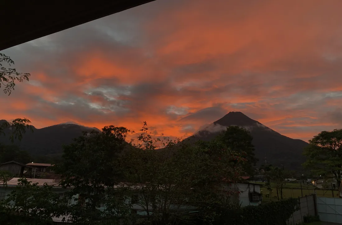 Arenal Volcano at sunset seen from the homes, with the garden and rooftops in front