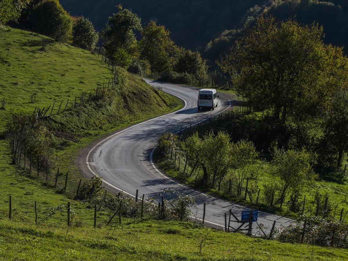 A vehicle rounding a curve on a paved road through green hills