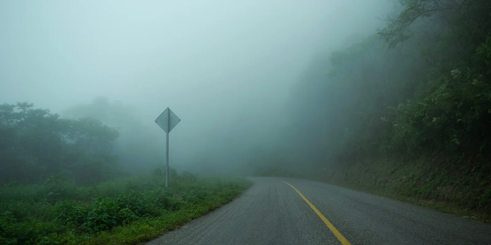 A paved mountain road disappearing into thick cloud