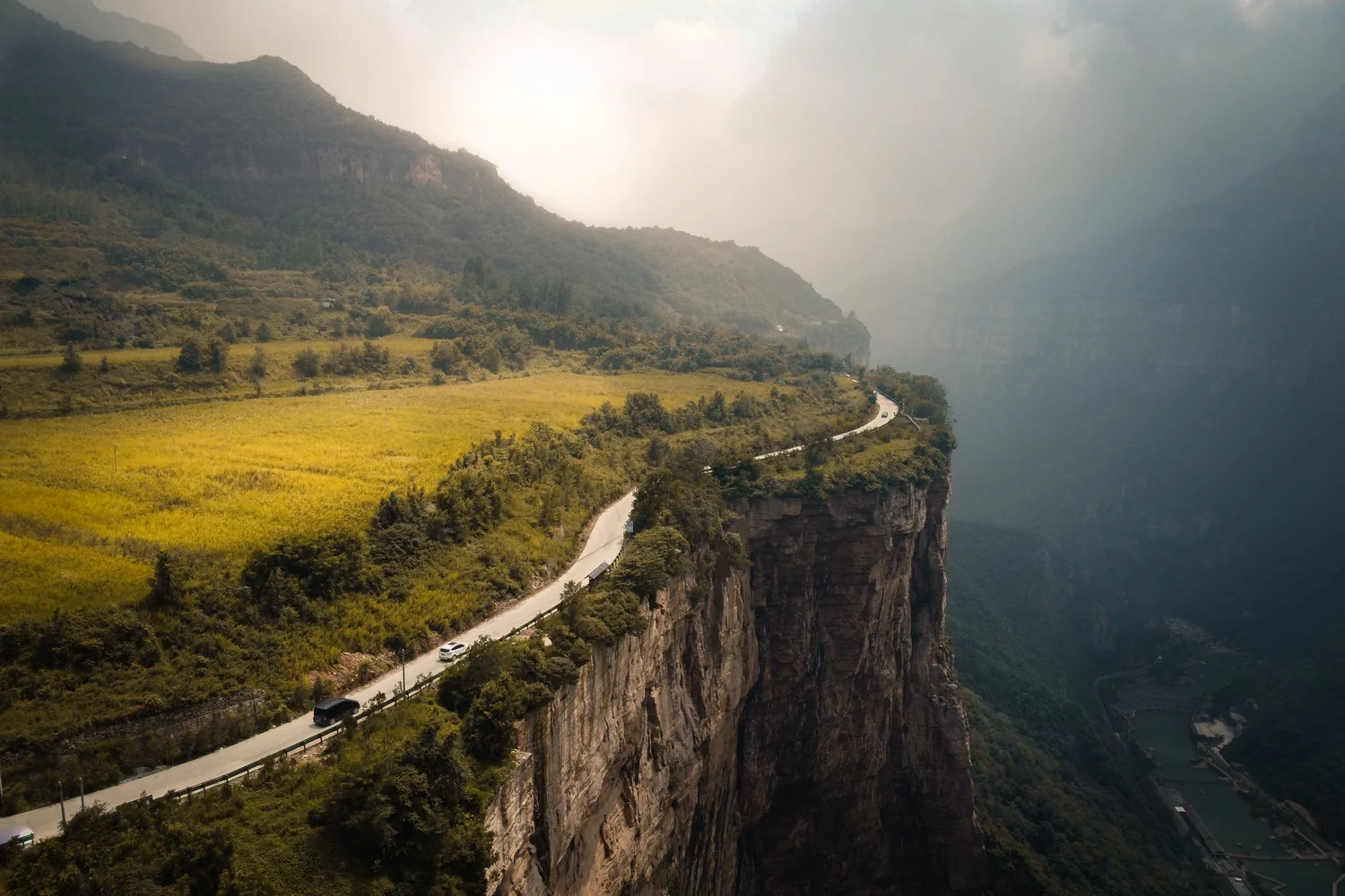 A narrow road cut into a cliff high above a valley, with no shoulder