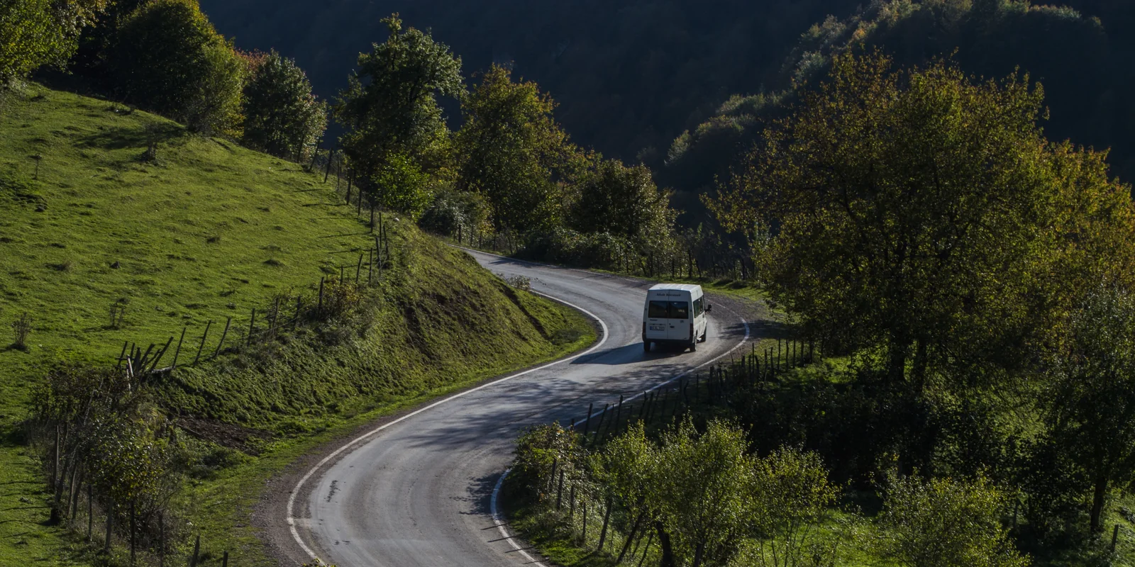 A white shuttle van on a winding road through green hills